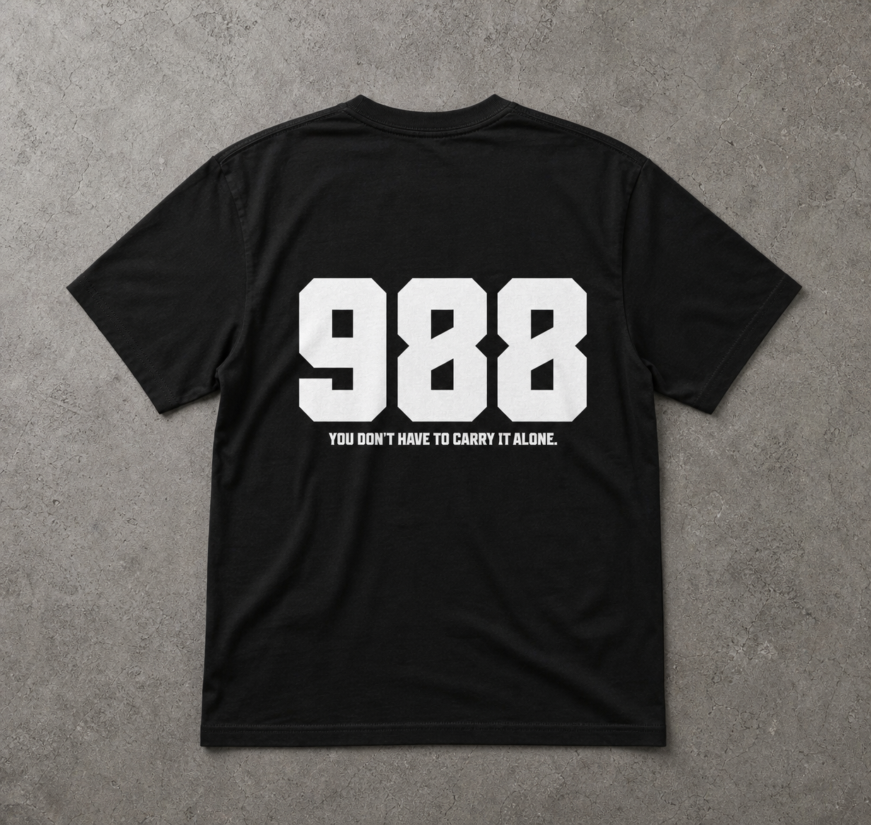 Black t-shirt with white text '988' and 'You don't have to carry it alone.' on a gray background