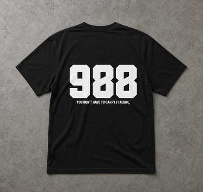 Black t-shirt with white text '988' and 'You don't have to carry it alone.' on a gray background