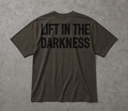 Dark gray t-shirt with 'LIFT IN THE DARKNESS' text on the back against a gray background