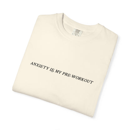 Folded beige t-shirt with 'ANXIETY IS MY PRE-WORKOUT' text on a white background