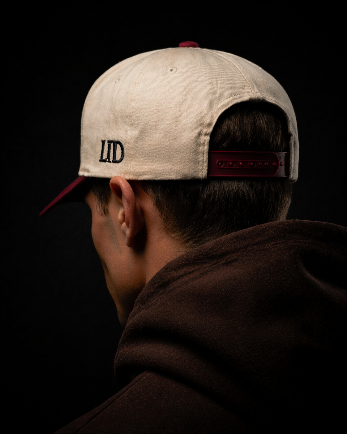 Person wearing a beige cap with 'LITD' logo on the back against a black background